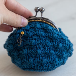 May include: A small blue crocheted coin purse with a metal clasp and a gold musical note charm.