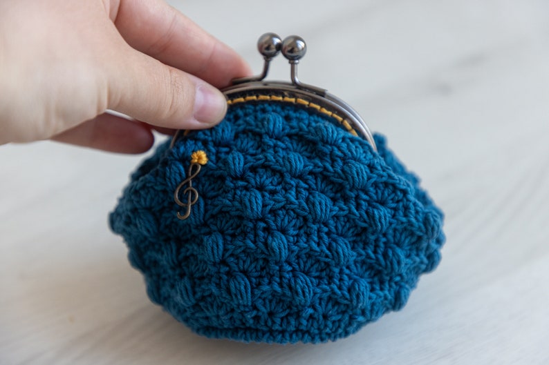 May include: A small blue crocheted coin purse with a metal clasp and a gold musical note charm.