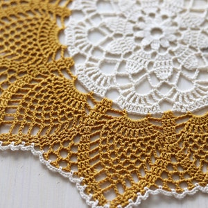 May include: A white and mustard yellow crocheted doily with a delicate floral pattern.
