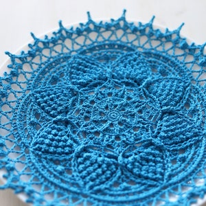 May include: A blue crocheted doily with a delicate floral pattern. The doily is circular and has a lacy edge.