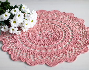 Puede incluir: Un encaje de ganchillo rosa con un delicado patrón floral. Margaritas blancas están dispuestas sobre el encaje.