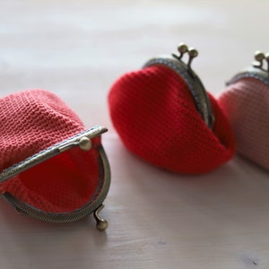 May include: Three crocheted coin purses with metal clasps. One purse is open and is red, the other two are closed, one is red and the other is pink.
