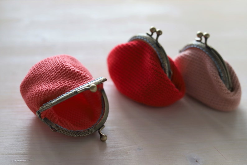 May include: Three crocheted coin purses with metal clasps. One purse is open and is red, the other two are closed, one is red and the other is pink.