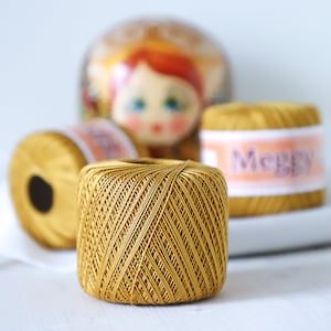 Może przedstawiać: Cztery szpulki złotej nici, jedna z etykietą z napisem "Merry" w różowych literach.