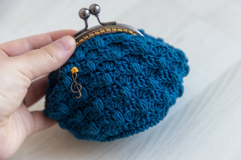 May include: A teal blue crocheted coin purse with a metal clasp and a gold musical note charm.