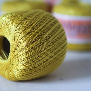 May include: A yellow ball of yarn with a hole in the center. The yarn is wound tightly and has a smooth, shiny finish.