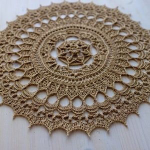 May include: A large, round, crocheted doily in a light brown color. The doily has a delicate, intricate design with a central motif.