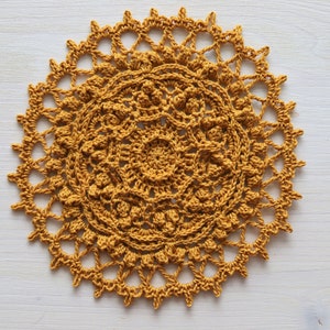 Peut inclure: Un napperon crocheté de couleur jaune moutarde. Le napperon a une forme circulaire avec un design détaillé et complexe.