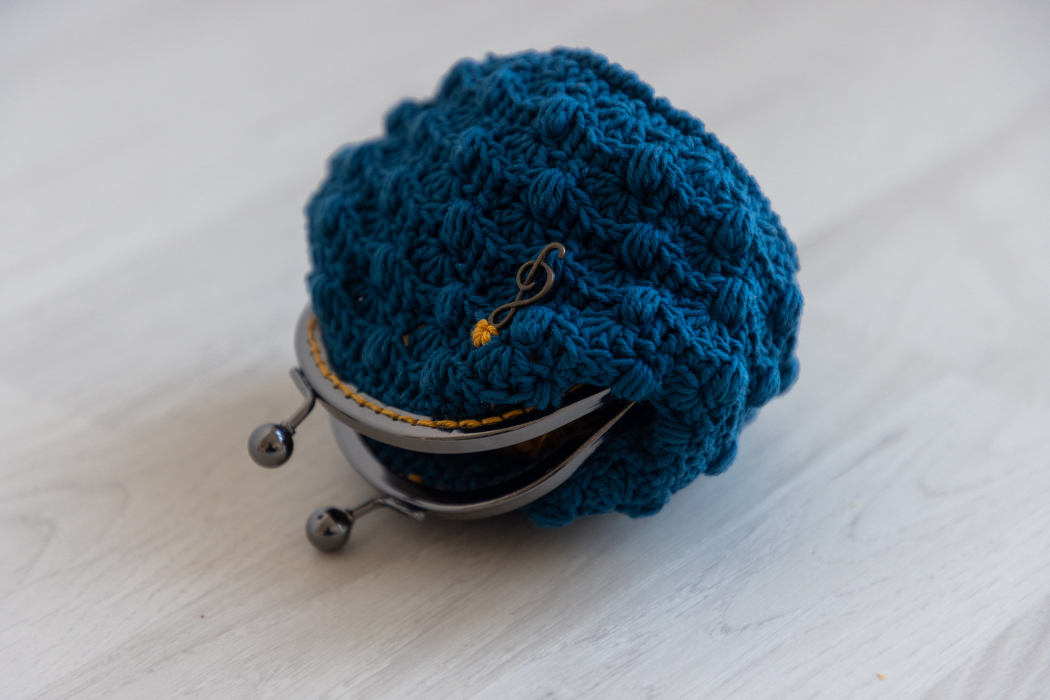 May include: A blue crocheted coin purse with a metal clasp and a gold musical note charm.