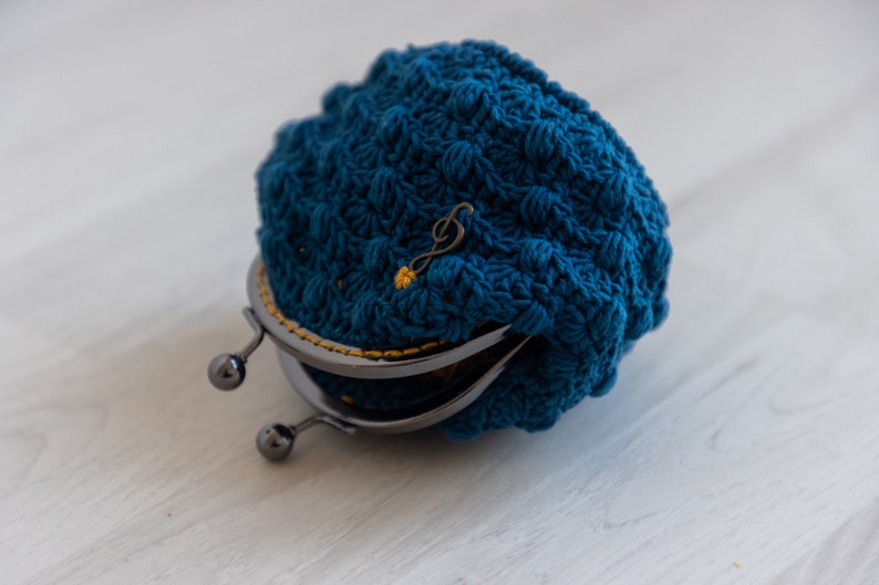 May include: A blue crocheted coin purse with a metal clasp and a gold musical note charm.