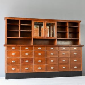 May include: A vintage wooden cabinet with a glass-door top section and a lower section with multiple drawers. The cabinet is made of dark wood with a natural finish and has brass hardware.