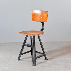 Può includere: Sedia in legno vintage con schienale e seduta curvi. La sedia ha una struttura in metallo scuro con base triangolare. La seduta e lo schienale sono in legno dai toni caldi, in contrasto con il metallo nero. Un mobile classico.