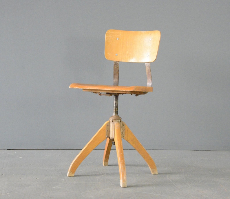 Op de afbeelding: Een vintage houten bureaustoel met een draaibare basis en verstelbare hoogte. De stoel heeft een lichte houtkleur en een eenvoudig ontwerp.