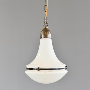 Op de afbeelding: Een witte glazen hanglamp met een messingkleurige bovenkant en een donkere metalen band. De lamp hangt aan een ketting en een gele draad. De lamp heeft een unieke, afgeronde vorm.