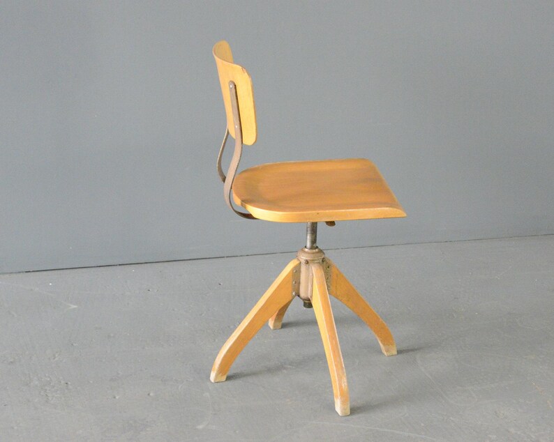 Op de afbeelding: Een houten draaistoel met een lichte houtkleur en een metalen onderstel. De stoel heeft een eenvoudig ontwerp met een gebogen rugleuning en een afgeronde zitting.