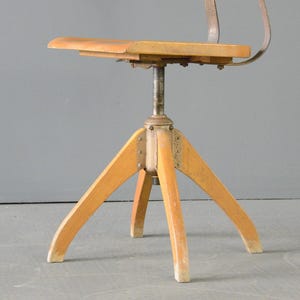 Op de afbeelding: Een draaibare houten stoel met een metalen frame en een driepootbasis. De stoel heeft een eenvoudig ontwerp en is gemaakt van natuurlijk hout.