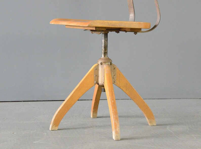 Op de afbeelding: Een draaibare houten stoel met een metalen frame en een driepootbasis. De stoel heeft een eenvoudig ontwerp en is gemaakt van natuurlijk hout.