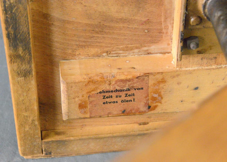 Op de afbeelding: Close-up van een houten doos met een label waarop staat "Zehnmechanik von Zeit zu Zeit etwas &ouml;len!" Het label is aan de binnenkant van de doos bevestigd.