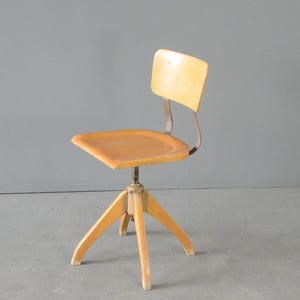 Op de afbeelding: Een draaibare stoel van licht hout met een metalen rugleuning en een vierpotig onderstel.