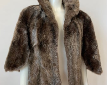 Könnte beinhalten: Eine braune Kunstfelljacke mit Schalkragen. Die Jacke hat kurze Ärmel und eine lockere Passform.