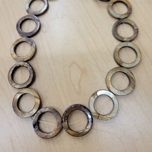 May include: A strand of brown and white shell beads strung on a clear thread. The beads are round and have a hole in the center. The beads are arranged in a circle.