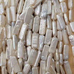 May include: A close-up of a pile of white rectangular pearl beads. The beads have an iridescent sheen and are arranged in a random pattern.