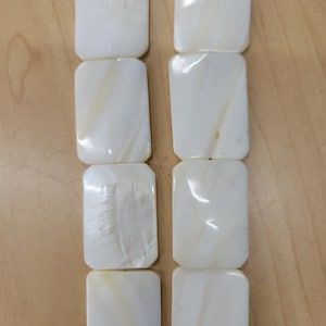 May include: A strand of white rectangular shell beads. The beads have a smooth, polished surface and a subtle iridescent sheen.