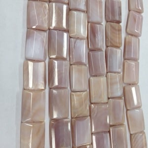 May include: Rows of rectangular beads in shades of peach, cream, and light brown. The beads have a polished, iridescent surface, and are strung together. The beads are square with rounded corners. The beads are likely for jewelry making.