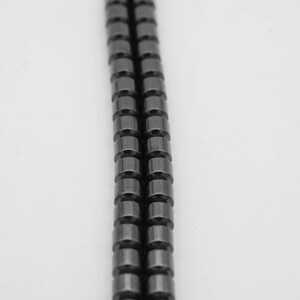 May include: A strand of black hematite beads, each bead is cylindrical in shape.
