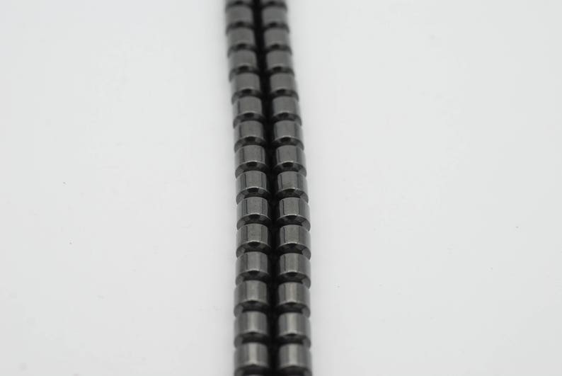 May include: A strand of black hematite beads, each bead is cylindrical in shape.