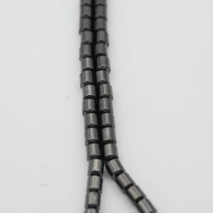 May include: A strand of black hematite beads, each bead is cylindrical in shape.