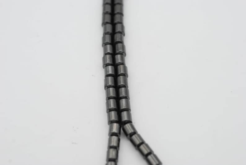 May include: A strand of black hematite beads, each bead is cylindrical in shape.