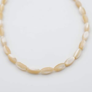 May include: A strand of oval-shaped, cream-colored shell beads.