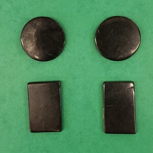 Può includere: Quattro pietre lisce di forma rettangolare e rotonda di colore nero. Le pietre sono disposte in due file di due.