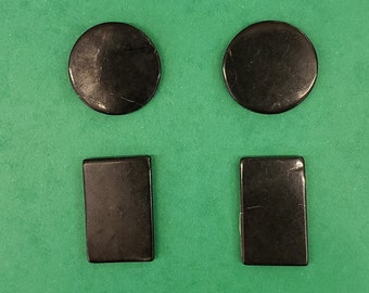 May include: Four black, smooth, rectangular and round shaped stones. The stones are arranged in two rows of two.