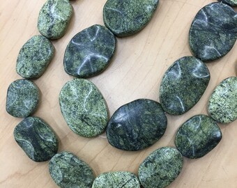 Könnte beinhalten: Eine Kette aus ovalen, grün-schwarzen Edelsteinen. Die Perlen sind glatt und poliert und haben ein geflecktes Muster.
