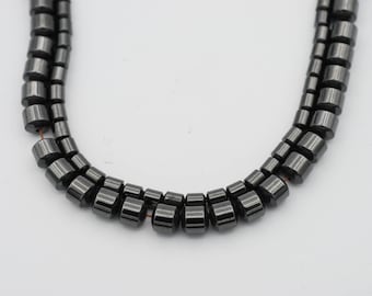 May include: A strand of black hematite beads, each bead is cylindrical and has a smooth, polished finish.