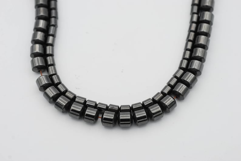 May include: A strand of black hematite beads, each bead is cylindrical and has a smooth, polished finish.