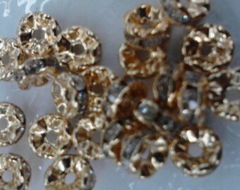 May include: A close-up of a pile of gold-colored metal beads with a clear crystal in the center of each bead.