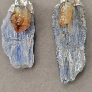 May include: Two blue kyanite pendants with a clear, yellow citrine crystal on top. Each pendant has a silver bail.