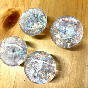 Peut inclure: Quatre boutons en verre iridescent avec un motif moucheté argenté et doré. Les boutons sont ronds et ont une finition lisse et polie.