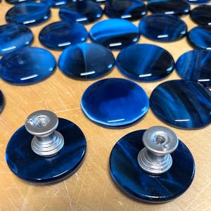 May include: A set of blue glass cabinet knobs with silver metal bases. The knobs are round and have a swirl pattern.