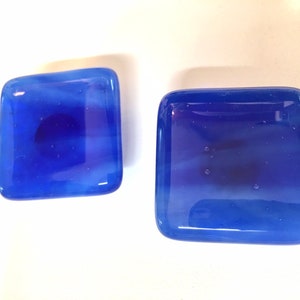 May include: Two small, square, blue glass dishes with a white swirl design. The dishes are made of clear glass with a blue tint and have a white swirl design.