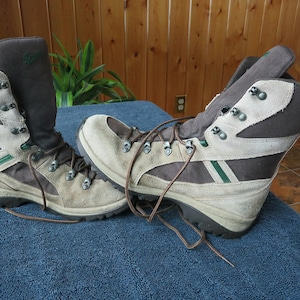 May include: A pair of hiking boots in tan, brown, and green. The boots have a high-top design with laces and metal eyelets. The boots are made of suede and fabric materials.