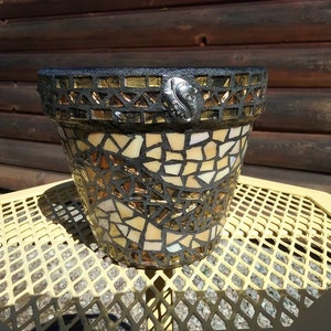 May include: A mosaic planter with a black base and a design of gold and white tiles. The planter has a decorative metal leaf accent.