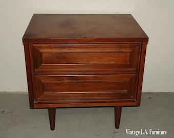 May include: A vintage wooden nightstand with two drawers and tapered legs. The drawers have a raised, detailed design.