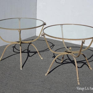May include: Two round glass-top tables with gold metal frames and decorative animal head accents on the legs. The tables are on a light gray carpet.