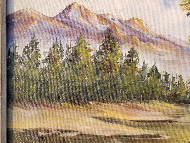 May include: A painting of a mountain range with snow-capped peaks in the background. A forest of pine trees is in the foreground. The sky is a light blue with some clouds.
