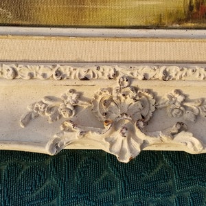 May include: A white ornate picture frame with a distressed finish. The frame has a decorative floral design and a raised edge.