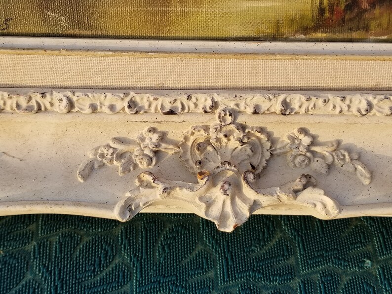 May include: A white ornate picture frame with a distressed finish. The frame has a decorative floral design and a raised edge.